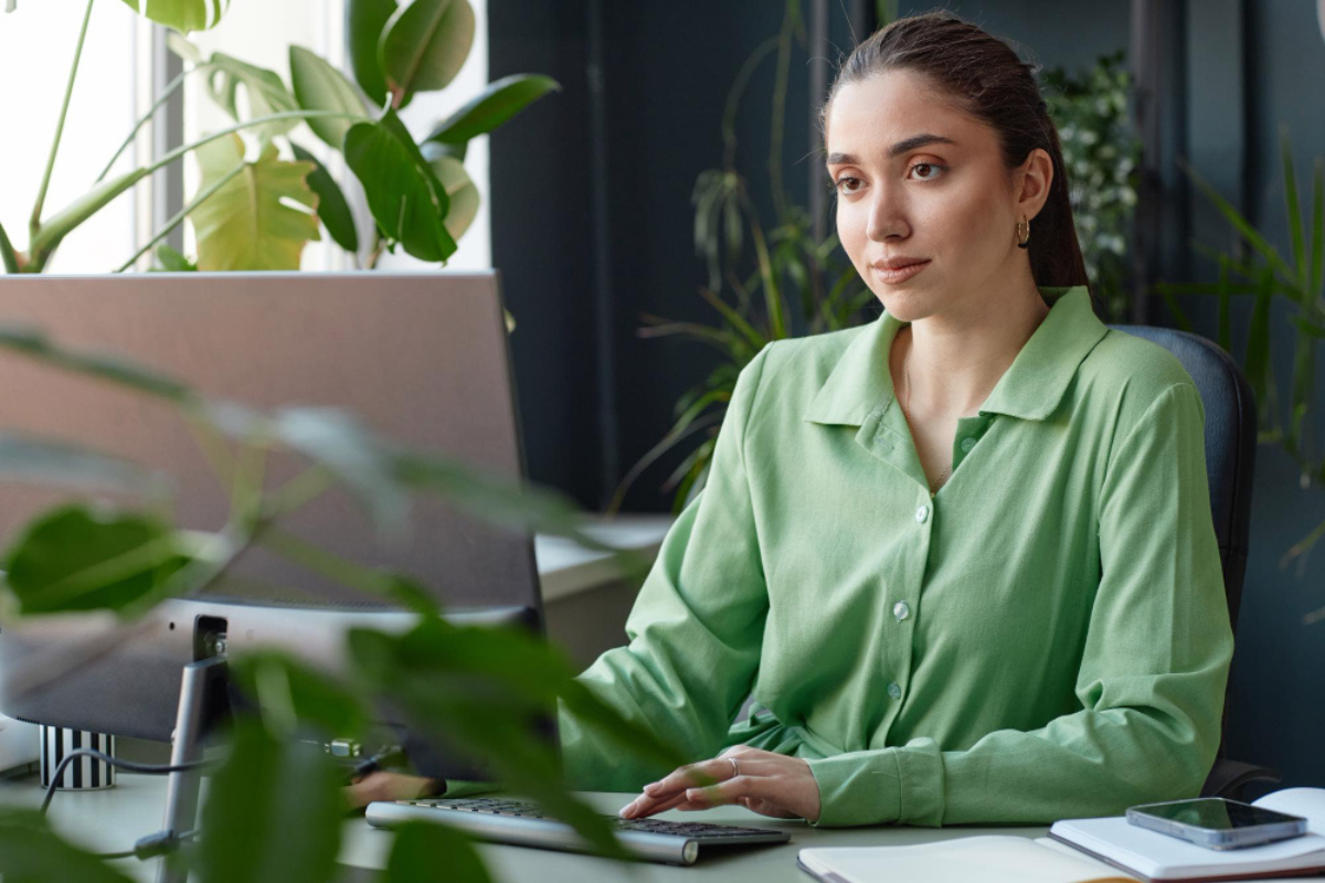 Mulher sentada mexendo em notebook sobre uma mesa em ambiente de escritório representando: Como garantir rastreabilidade e controle de acesso em documentos digitais.
