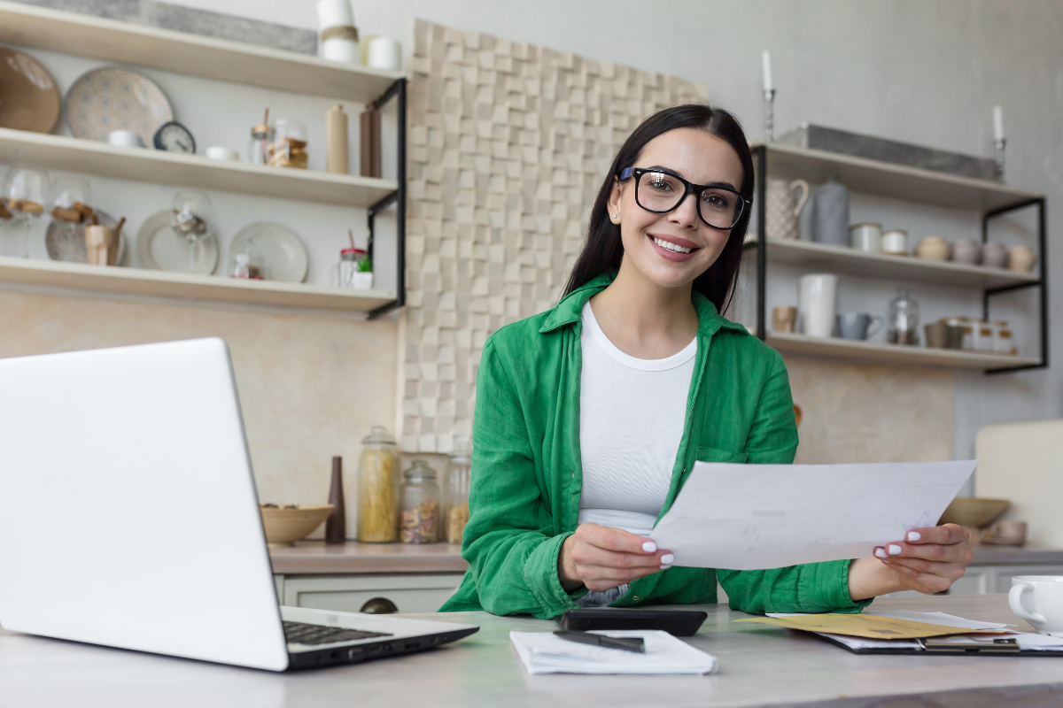 Mulher em frente ao notebook segurando documento relacionado ao e-CNPJ A1, utilizado para emissão segura de nota fiscal eletrônica.