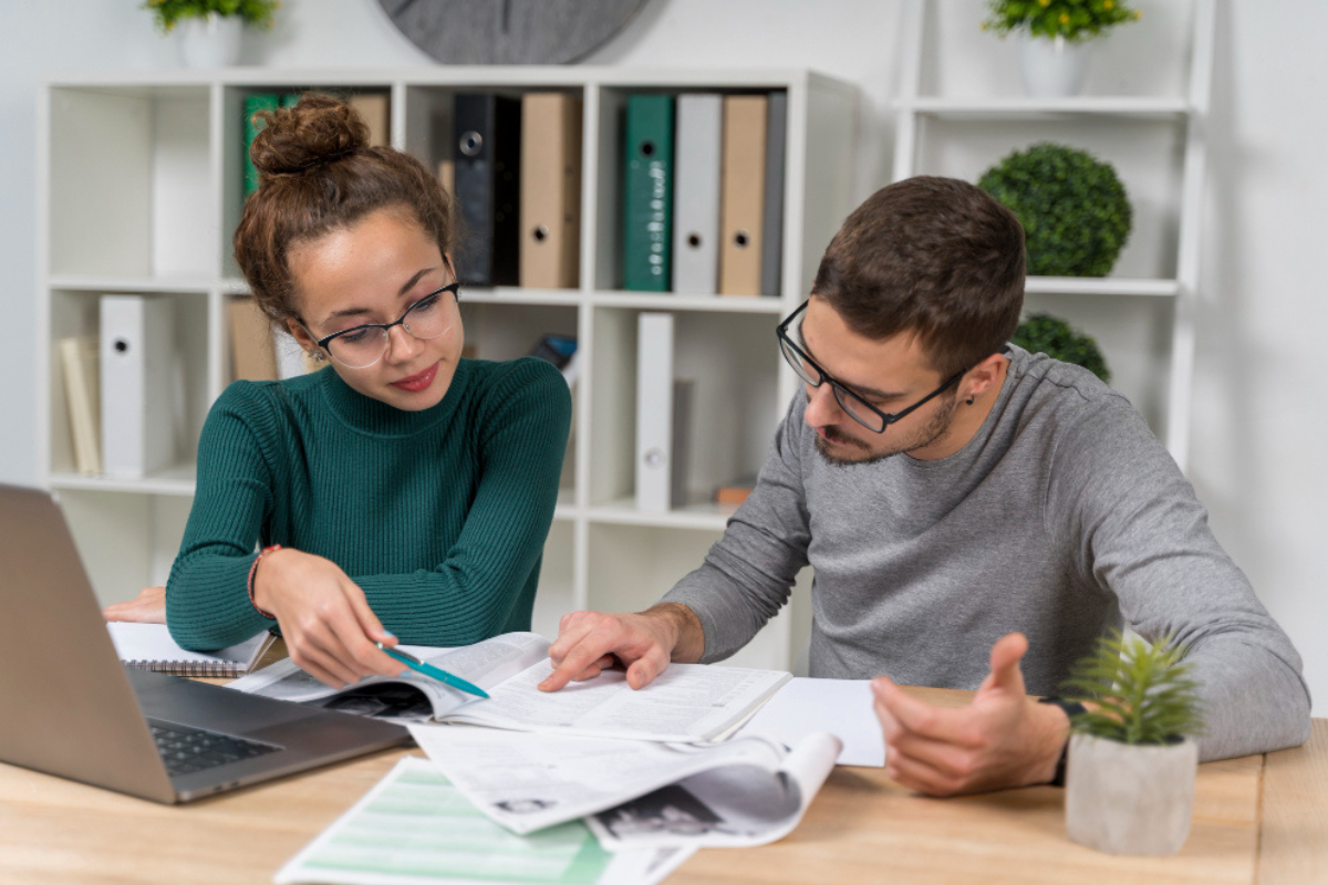 Casal em ambiente de escritório residencial sentados em frente a um notebook em uso sobre uma mesa fazendo anotações em um caderno e ao mesmo tempo lendo outro caderno de anotações e outros documentos representando: Certificado digital gratuito vale a pena? Veja os riscos e limitações.