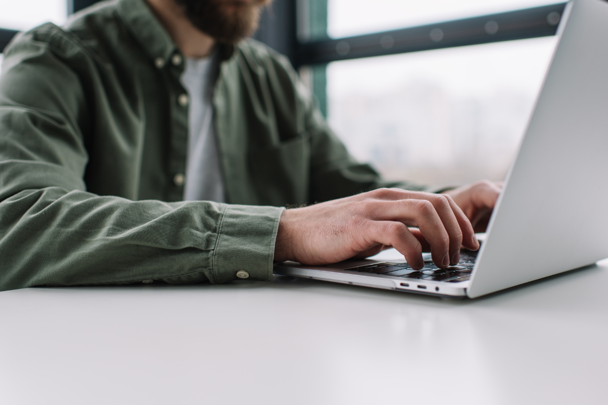 Homem sentado usando notebook sobre uma mesa em ambiente de escritório representando: Imposto Seletivo (IS): guia completo sobre o novo imposto.