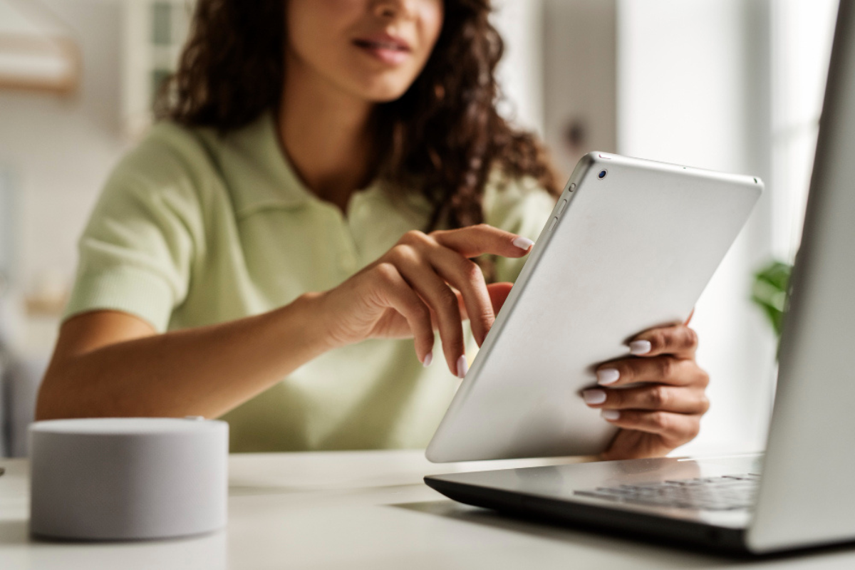 Mulher sentada em frente um notebook usando um tablet sobre uma mesa com uma xícara de café ao lado em um ambiente de escritório representando: Reforma tributária 2026: o que você precisa saber?