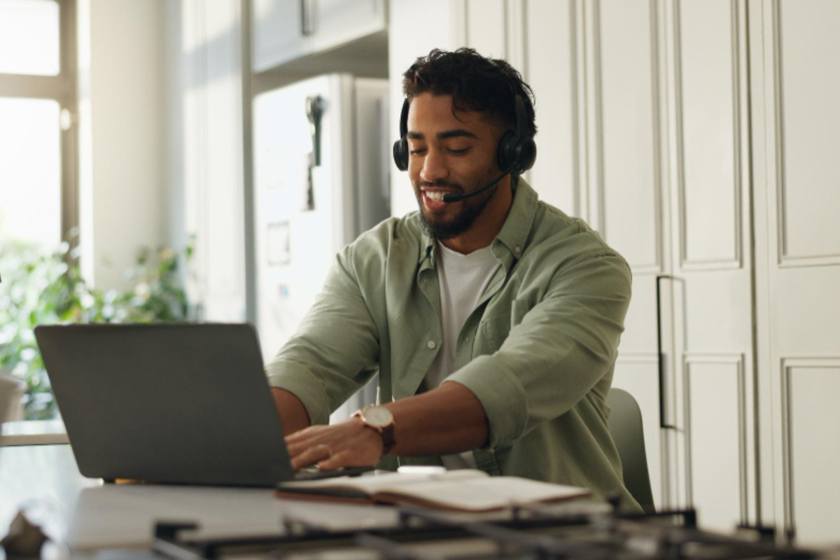 Homem sentado usando fone e notebook sobre uma mesa com agenda aberta ao lado em ambiente de sala de estar em home office representando: Fim do SAT-SP: você precisa de um certificado digital para emitir NFC-e?
