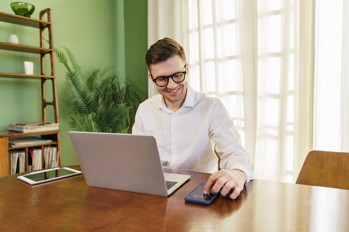 Homem sentado em frente a um notebook sobre mesa usando também celular ao lado em ambiente de escritório representando: Como o PIS/Cofins será substituído?