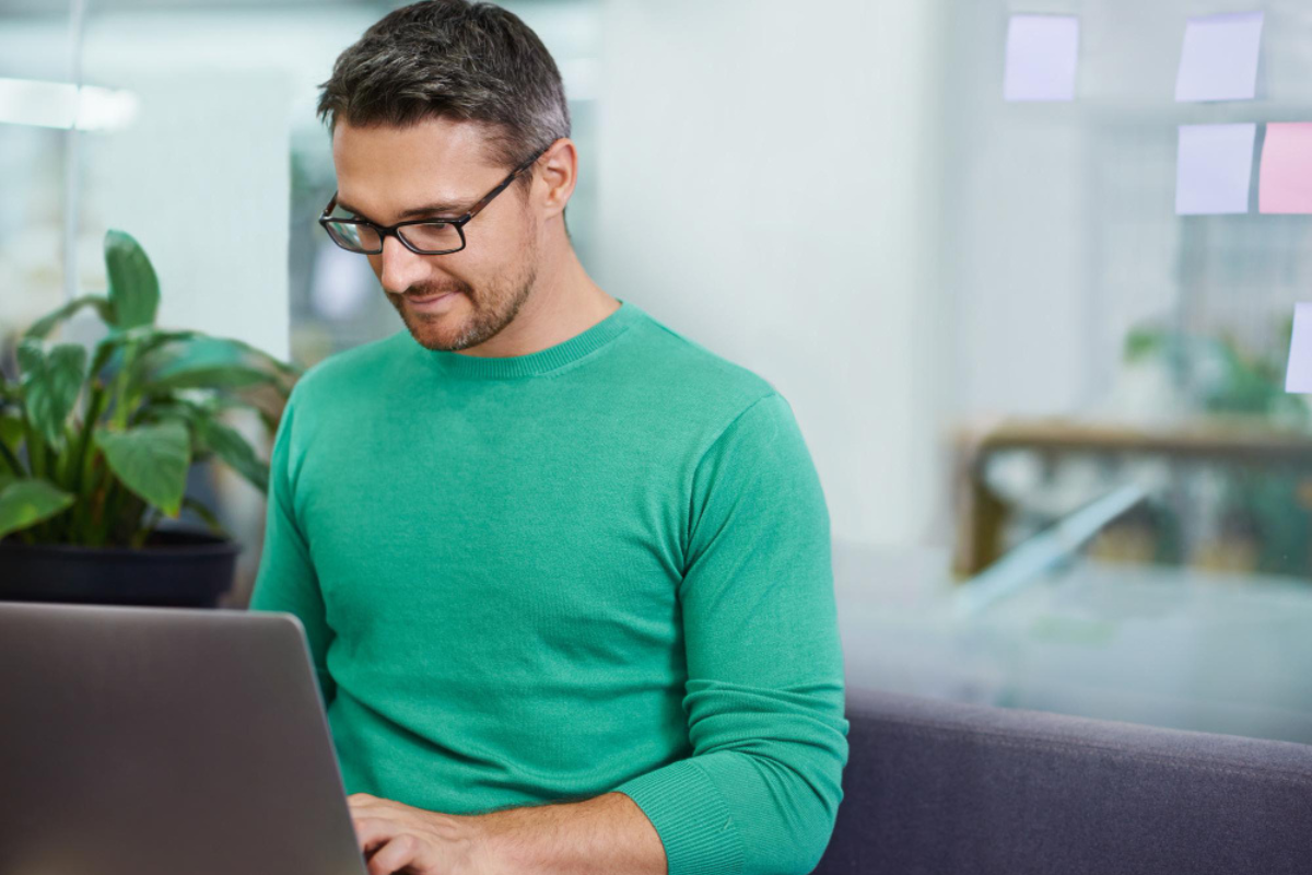 Homem sentado trabalhando em um notebook sobre uma mesa em ambiente de escritório representando: Obrigações acessórias: o que são e o que muda na Reforma Tributária.