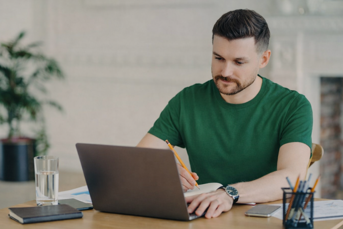 Homem usando notebook sobre uma mesa sentado em ambiente home office representando: Como funcionam as multas por notas emitidas sem IBS e CBS?
