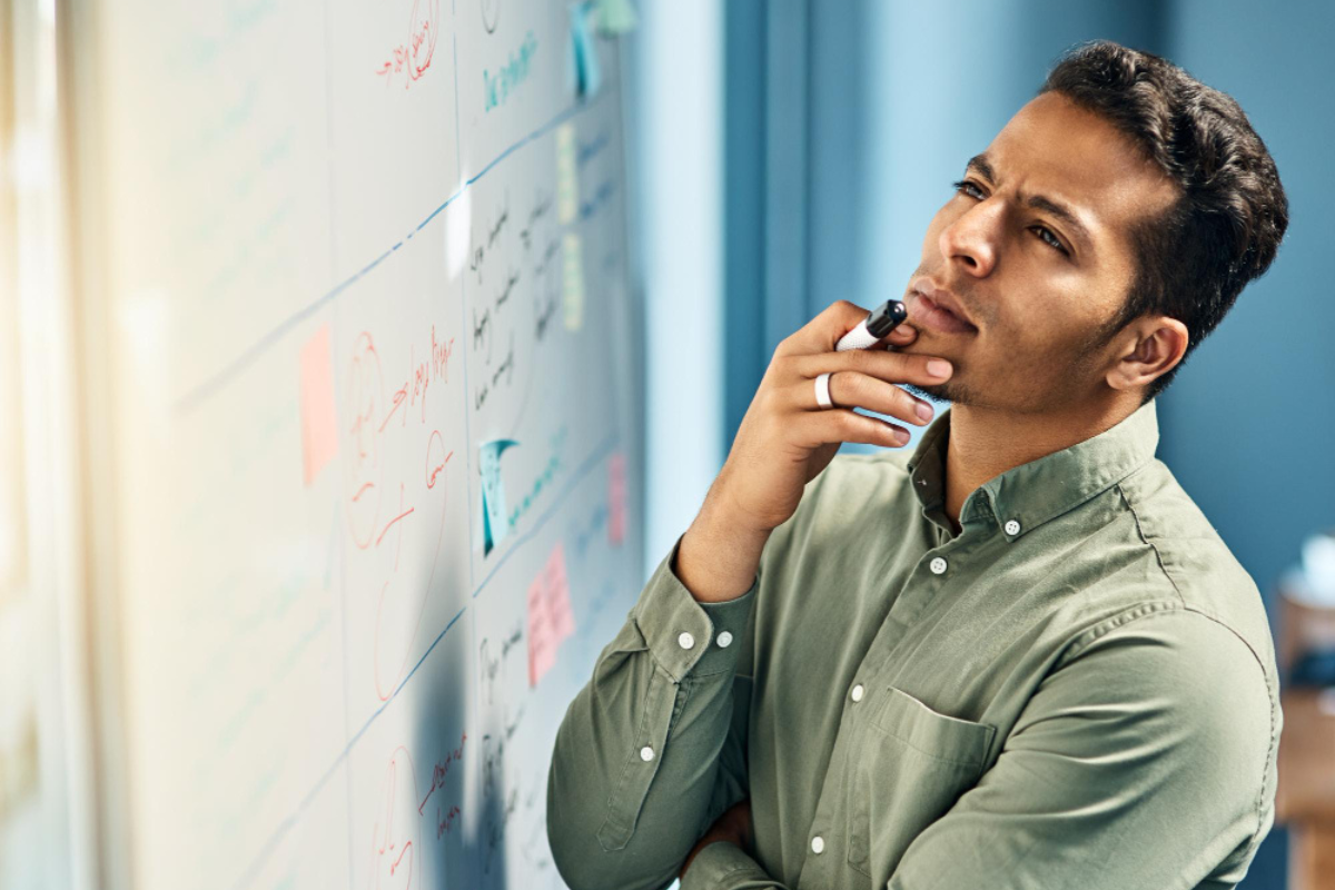 Homem em ambiente de sala de reunião em frente a um quadro negro analisando dados e anotações no mesmo representando: Calendário fiscal da empresa: como saber o que é realmente importante.