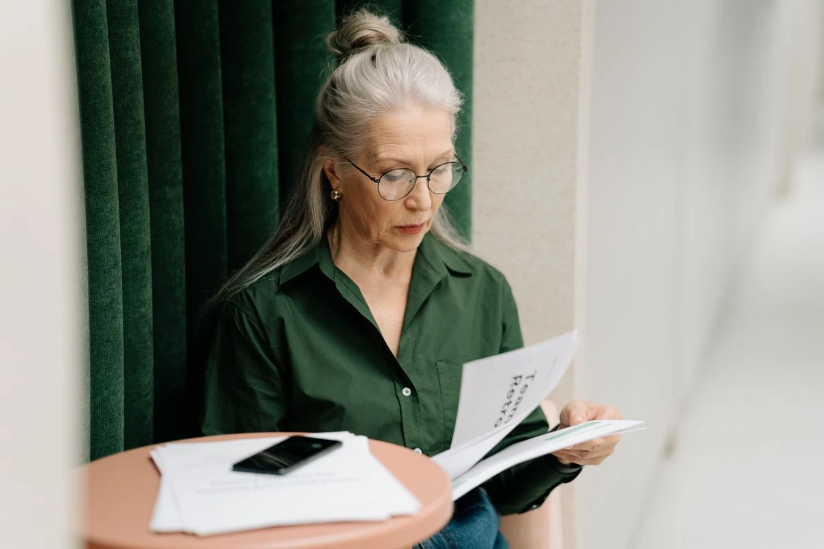 Mulher empresária de pé lendo documentos em mãos sobre Como estruturar um fluxo de renovação de certificados para não perder prazos de nenhum cliente? Em ambiente de escritório particular.